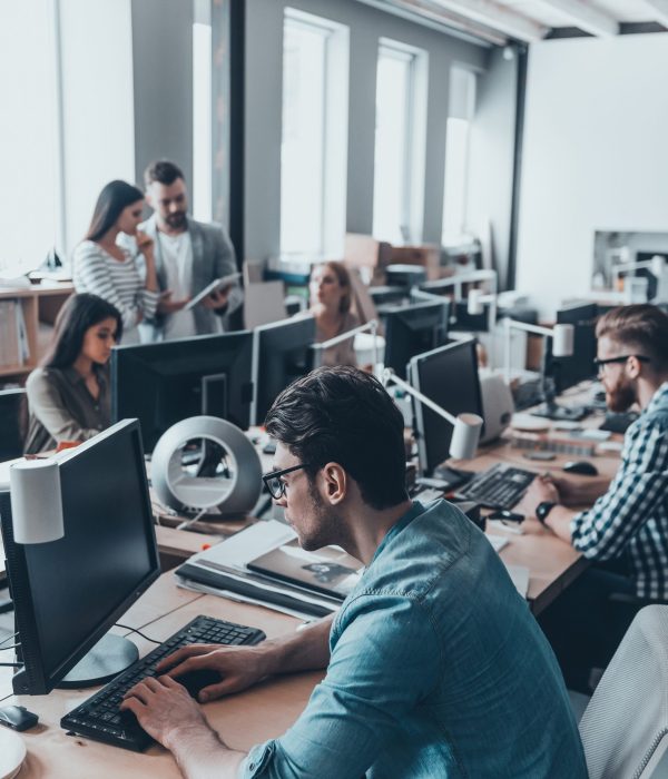 Busy working day. Group of young business people in smart casual wear working and communicating while sitting at the large desk in the office together
